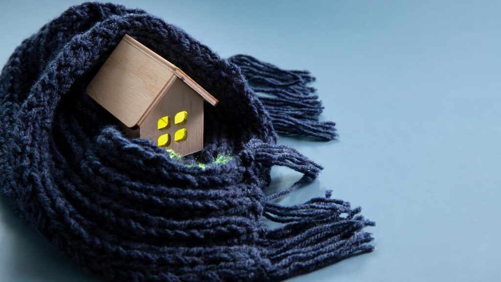 une maison en bois avec une écharpe qui l'a protège, qui représente la protection des logements pendants l'hiver, la protection contre les coupures d'électricité et gaz